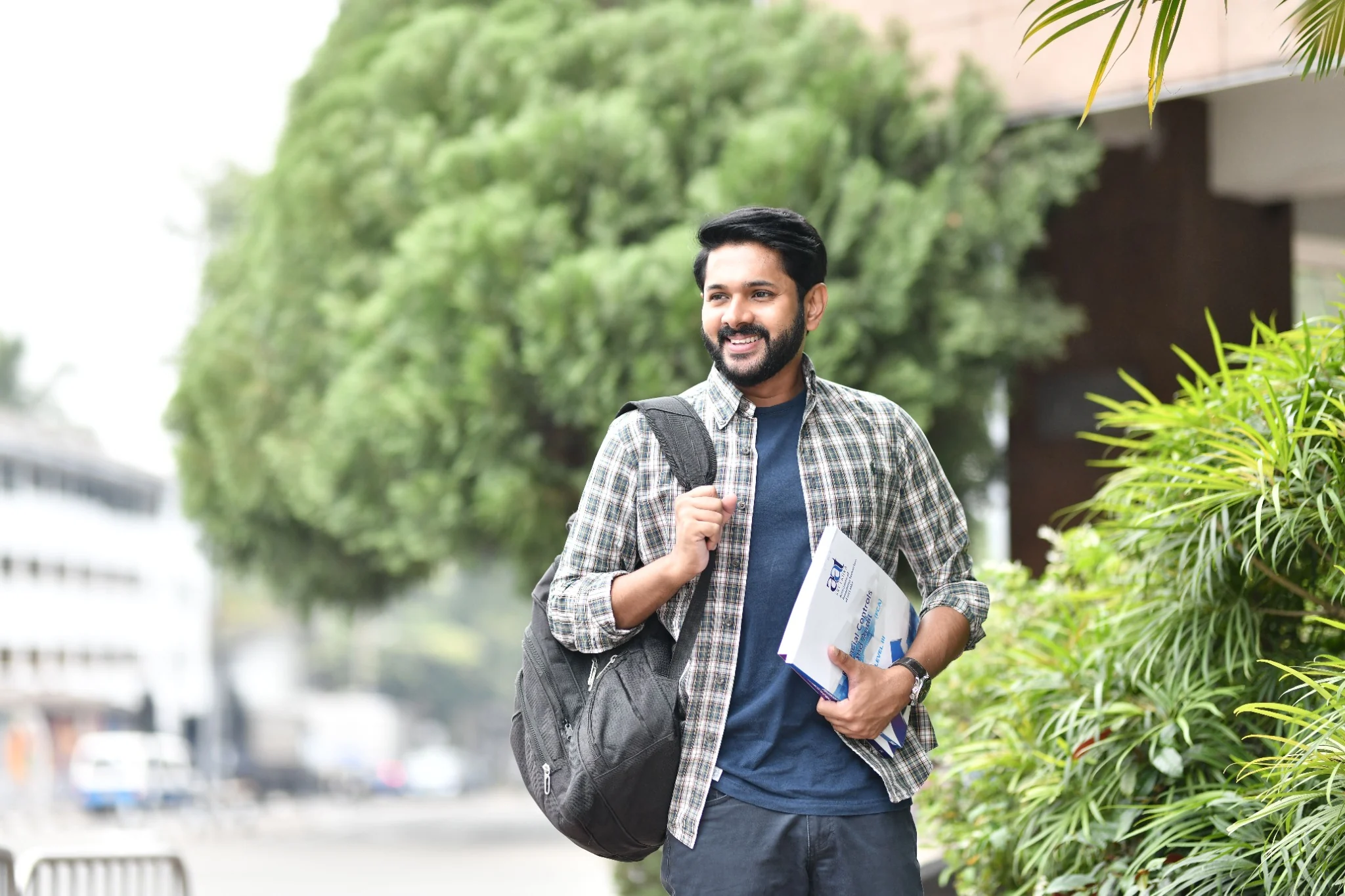 Indian college student carrying books and a backpack on a leafy campus